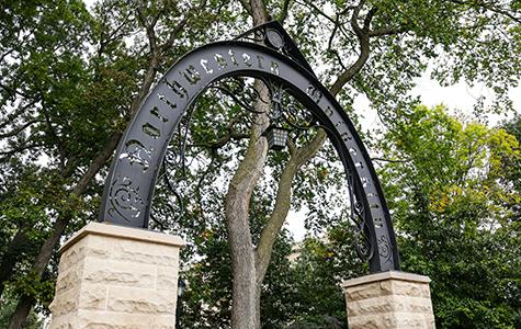 An arch with the words Northwestern University written across it (known as Weber Arch) with trees in the background.
