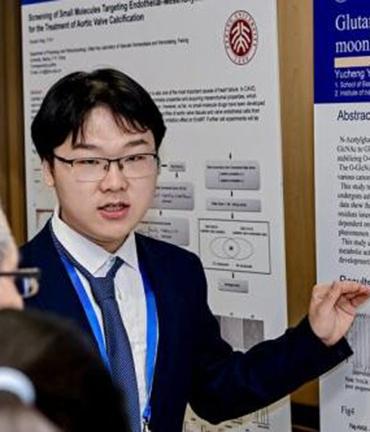 Yuchen Yin standing in front of his poster explaining his research.